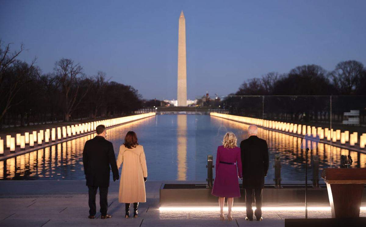 From left to right: Douglas Emhoff, U.S. Vice President-elect Kamala Harris, Dr. Jill Biden and U.S. President-elect Joe Biden look down the National Mall as lamps are lit to honor the nearly 400,000 American victims of the coronavirus pandemic at the Lincoln Memorial Reflecting Pool January 19, 2021 in Washington, DC. As the nation’s capital has become a fortress city of roadblocks, barricades and 20,000 National Guard troops due to heightened security around Biden’s inauguration, 200,000 small flags were installed on the National Mall to honor the nearly 400,000 Americans killed by COVID-19.