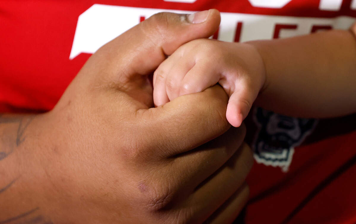 N.C. State defensive lineman Joshua Harris holds the hand of his 9-month-old daughter Aylah at the Murphy Center in Raleigh, N.C., Thursday, June 16, 2022.