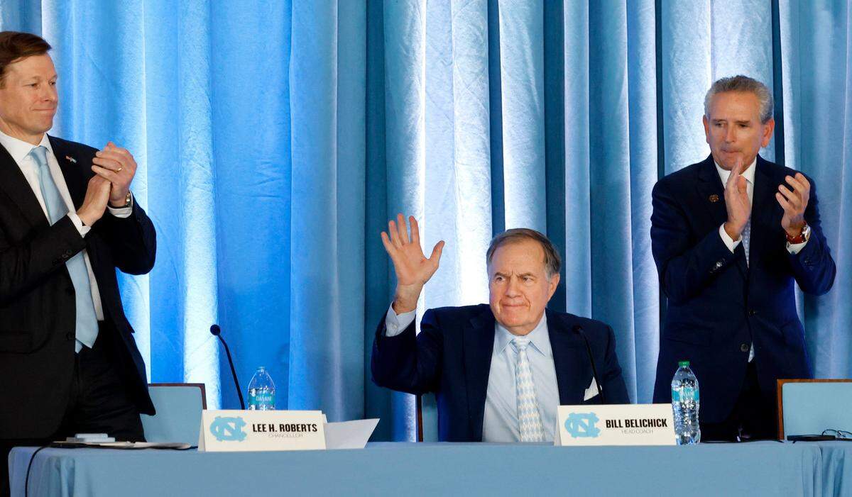 New North Carolina head football coach Bill Belichick acknowledges the crowd at the start of the press conference announcing his hiring at the Loudermilk Center for Excellence at UNC in Chapel Hill, N.C., Thursday, Dec. 12, 2024. Chancellor Lee Roberts stands to the left and AD Bubba Cunningham stands to the right.