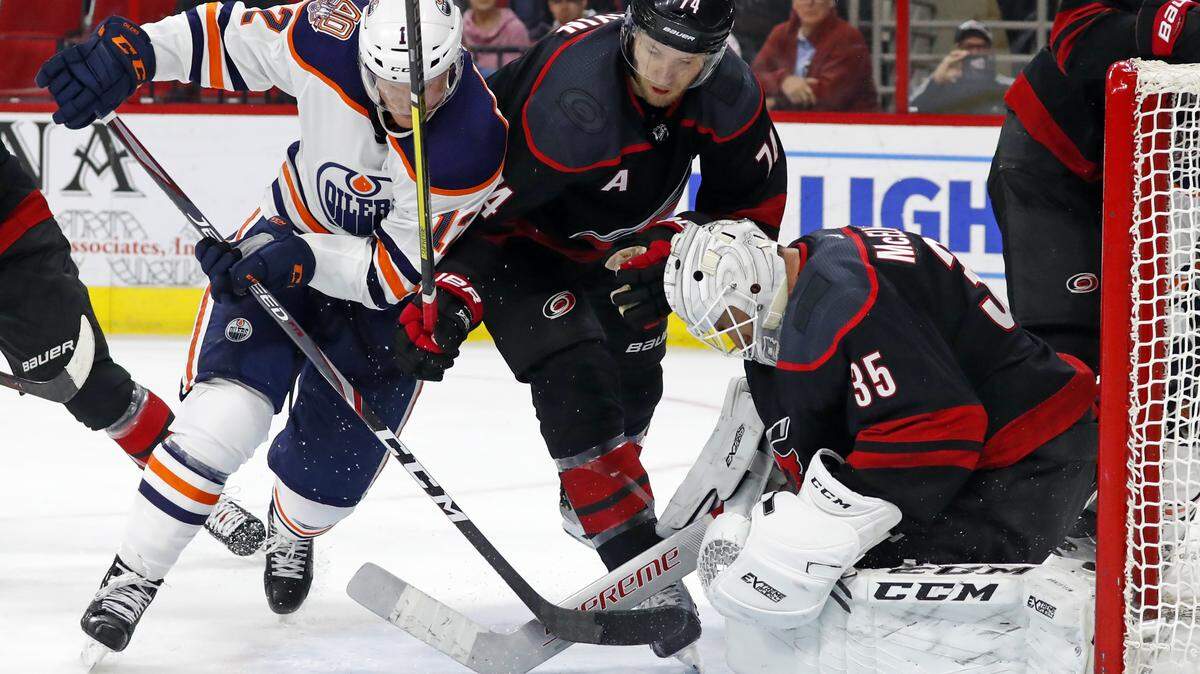 Edmonton Oilers’ Colby Cave (12) and Carolina Hurricanes’ Jaccob Slavin (74) battle in front of goaltender Curtis McElhinney (35) during the third period of an NHL hockey game, Friday, Feb. 15, 2019, in Raleigh, N.C. (AP Photo/Karl B DeBlaker)