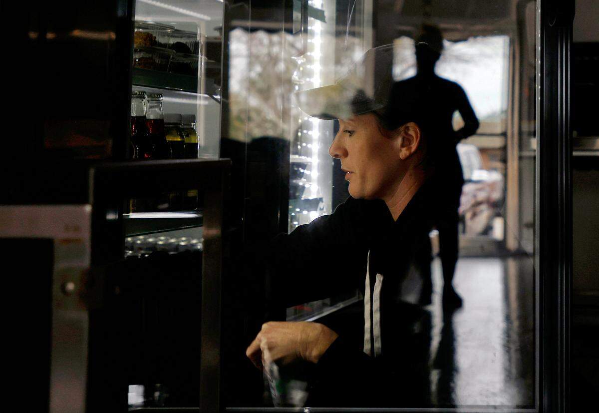 Rachel Haviley, owner of Limitless Meal Supply, restocks a refrigerated case while powering her business on a generator during a power outage on Monday, Dec. 5, 2022, in Carthage, N.C.