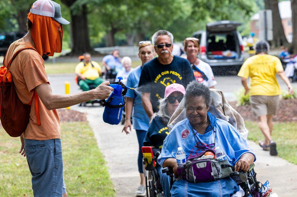 Joe Tate, a personal care assistant, mists Karen Burrison, among demonstrators rallying outside the North Carolina Department of Health and Human Services on Monday, June 24, 2024. About 50 demonstrators with National ADAPT rallied outside the office to mark the 25th Anniversary Rally of the Olmstead Decision in North Carolina.