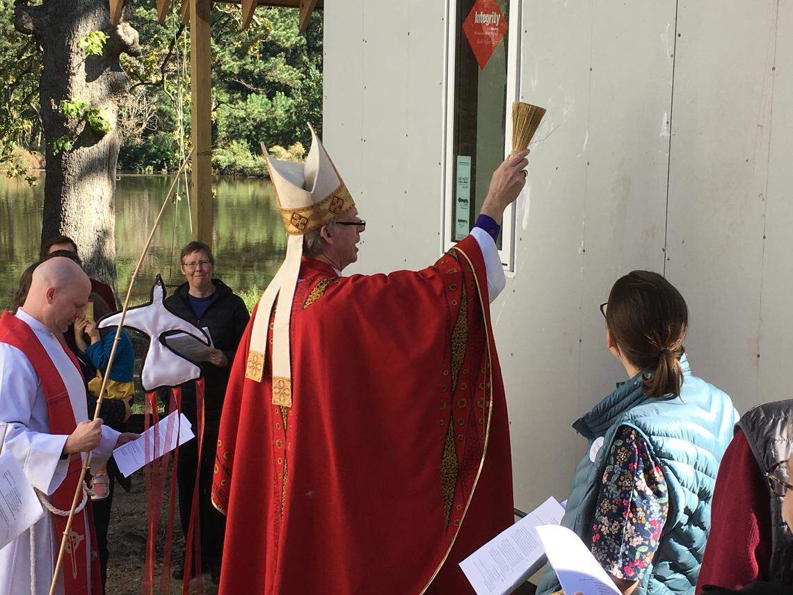 The Rt. Rev. Samuel Sewall Rodman III, the bishop of the Episcopal Diocese of North Carolina, uses an aspergillum dipped in holy water to bless one of three Pee Wee Homes being built on the campus of the Episcopal Church of the Advocate in Chapel Hill on Sunday.