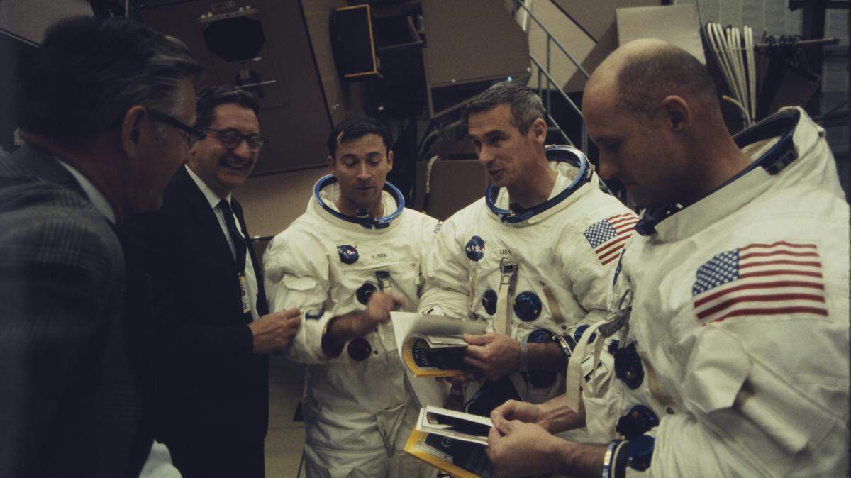 From the National Geographic Channel documentary “Apollo: Missions to the Moon,” astronauts Stafford, Young and Cernan read an article about an Apollo flight in National Geographic as two officials look on.