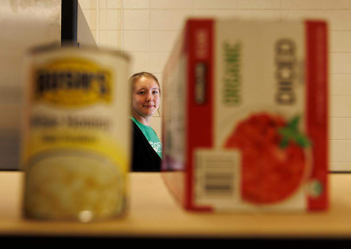 Nora Dicker, program manager for Porch Hillsborough, is photographed through food items at a pantry on Thursday, Nov. 14, 2024, in Hillsborough, N.C. The organization has experienced lower-than-normal nonperishable food collections since Hurricane Helene.