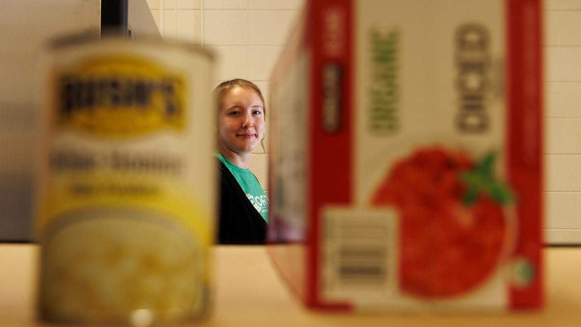 Nora Dicker, program manager for Porch Hillsborough, is photographed through food items at a pantry on Thursday, Nov. 14, 2024, in Hillsborough, N.C. The organization has experienced lower-than-normal nonperishable food collections since Hurricane Helene.