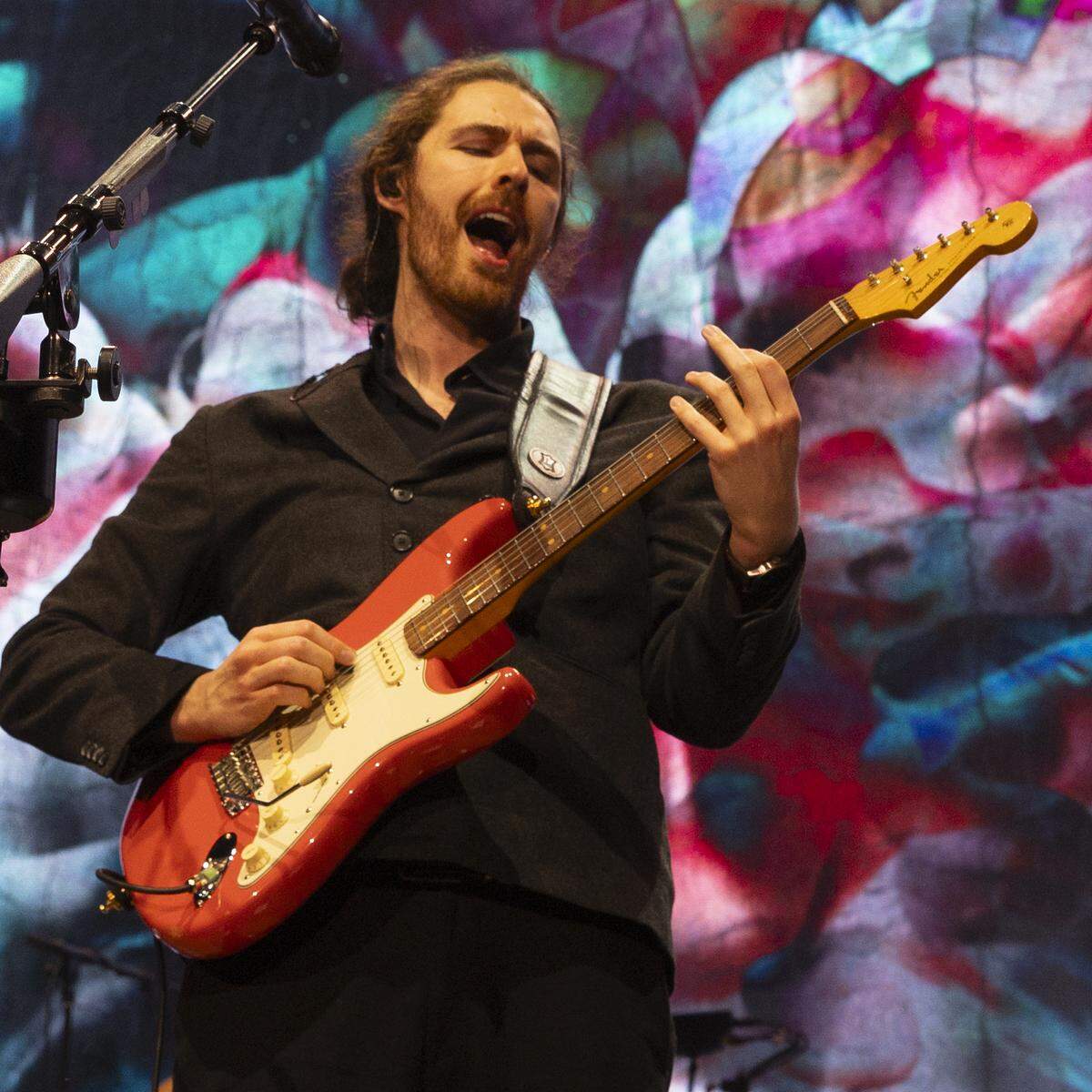 A background of swirling colors frames Hozier in concert at Coastal Credit Union Music Park at Walnut Creek in Raleigh, N.C., Saturday night, April 20, 2024.