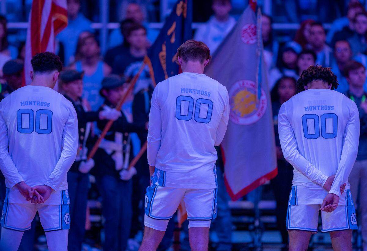 North Carolina players Creighton Lebo (14), Paxson Wojcik (8) and R.J. Davis (4) stand together during a moment of silence and tribute to Eric Montross prior to their game against Charleston Southern on Friday, December 29, 2023 at the Smith Center in Chapel Hill, N.C. Montross who played at North Carolina and was a color commentator, died of cancer on December 17, 2023.