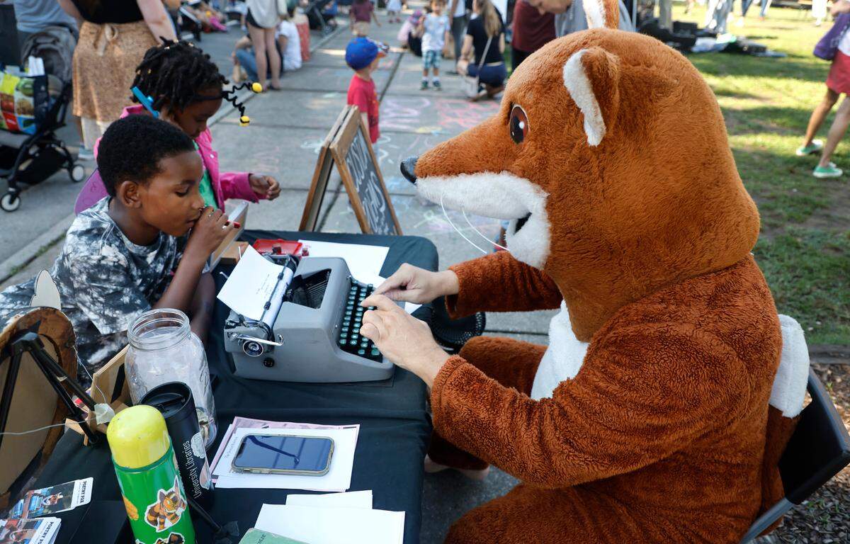 Chris Vitiello, otherwise known as the Poetry Fox, writes a poem for Tiberius Goddard, 8, at the Hunt Street Art and Food Truck Market in Durham, N.C., Saturday morning, June 24, 2023. Goddard’s sister, Tahira, stands next to him.