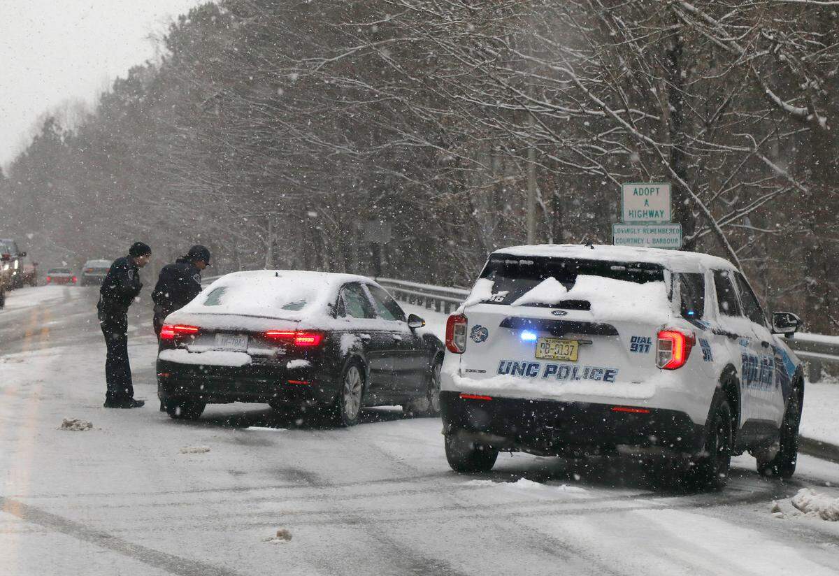 Law enforcement officers help a stalled vehicle on Manning Drive as snow falls in Chapel Hill, N.C. on Wednesday, Feb. 19, 2025.