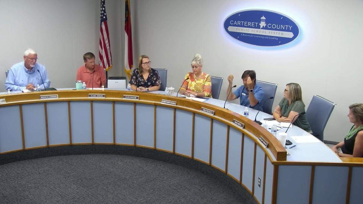 Carteret County school board member Travis Day holds up his hands to do the money gesture at the June 13, 2024 meeting as he accuses the tourism industry of blocking changes to North Carolina’s school calendar law