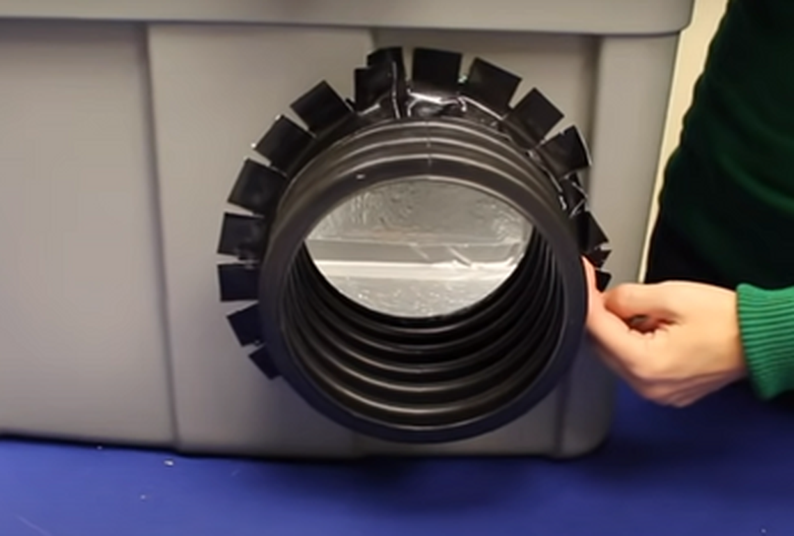 Duct tape, snipped every inch or two to accommodate the curve, is used to hold a flower pot liner in place on a cat shelter built from a plastic tote. The flower pot liner makes a tunnel that serves as an entrance.