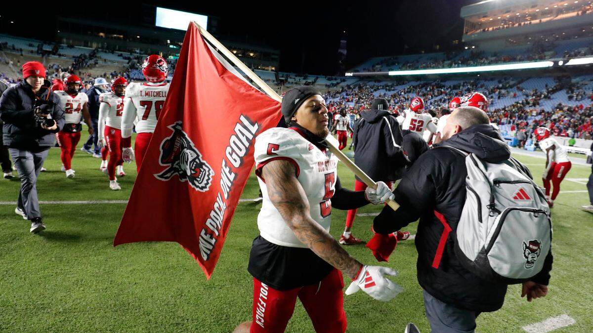 N.C. State’s DK Kaufman (5) walks the field with a Wolfpack flag after N.C. State’s 35-30 victory over UNC at Kenan Stadium in Chapel Hill, N.C., Saturday, Nov. 30, 2024.