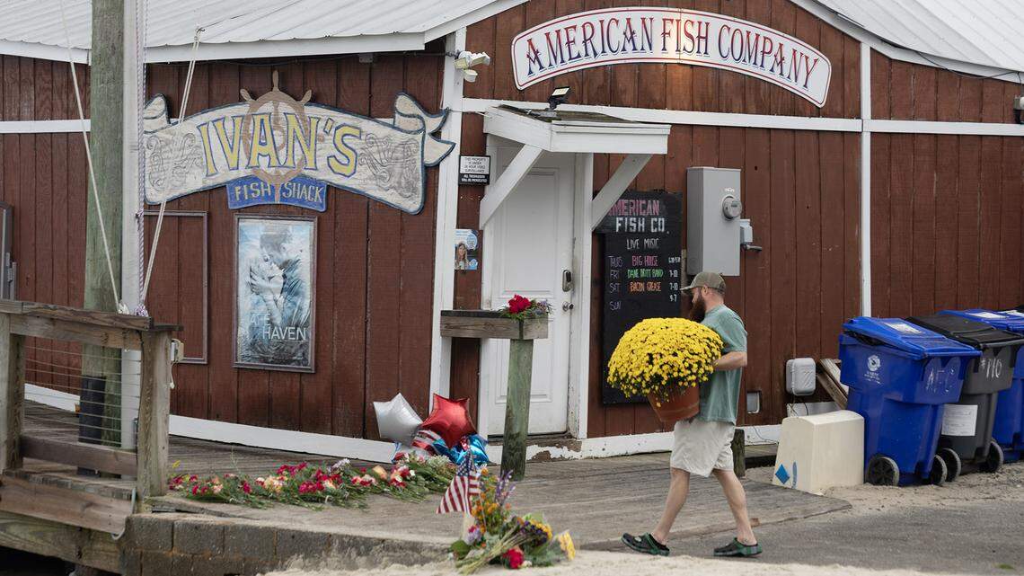 A man carries a large pot of flowers to a memorial outside of the American Fish Company where three people were shot and killed by a man in a boat on the water by the popular nightspot in Southport, N.C. Saturday night.