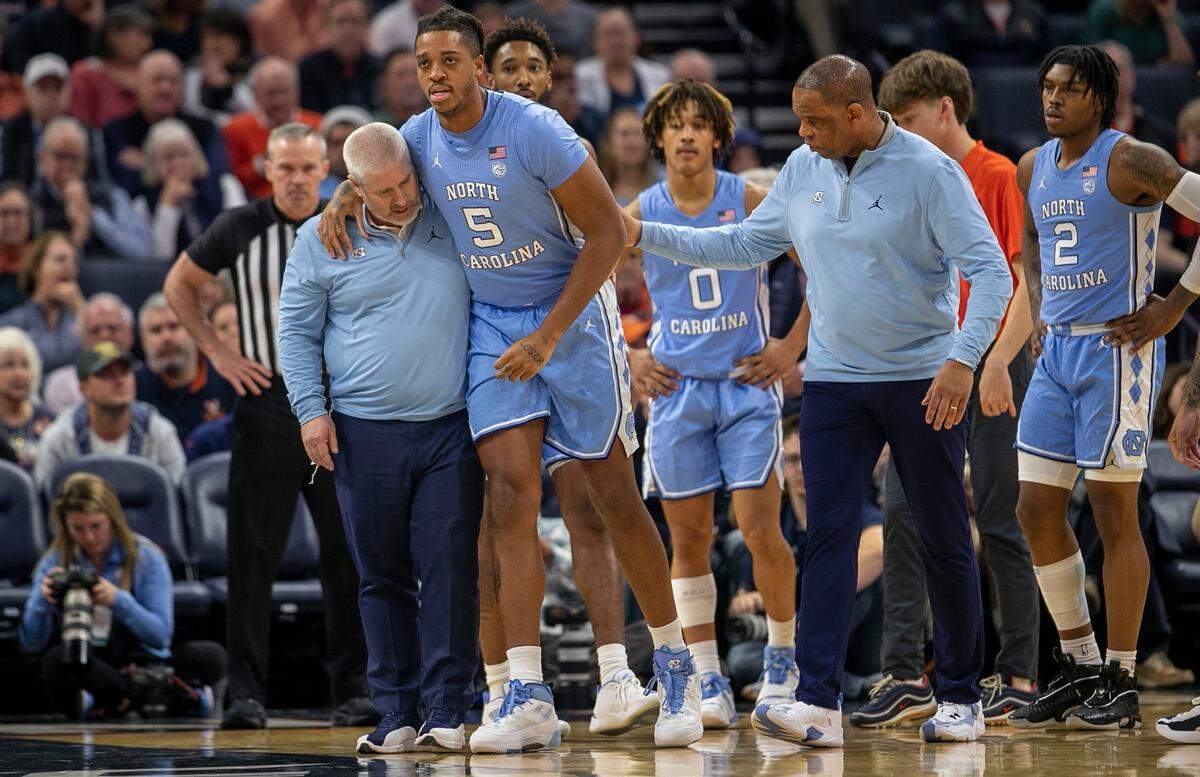 North Carolina trainer Doug Halverson and coach Hubert Davis help Armando Bacot (5) off the court after an injury in the opening minutes of play against Virginia on Tuesday, January 10, 2023 at John Paul Jones Arena in Charlottesville, Va.