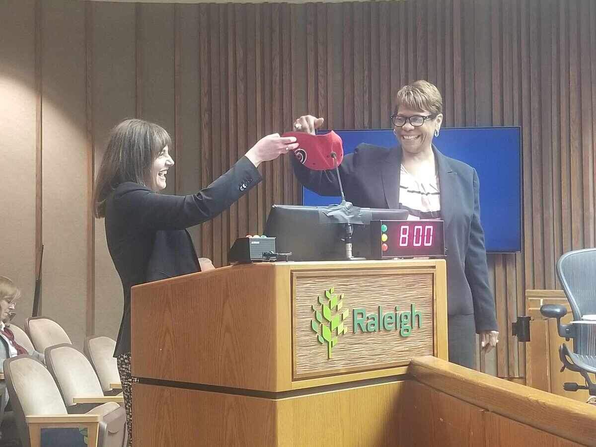 Raleigh City Attorney Karen McDonald pulls a district out of Carolina Hurricanes hat, held by Janie Richardson, to see which Raleigh City Council districts will move to a four-year term first in 2026.
