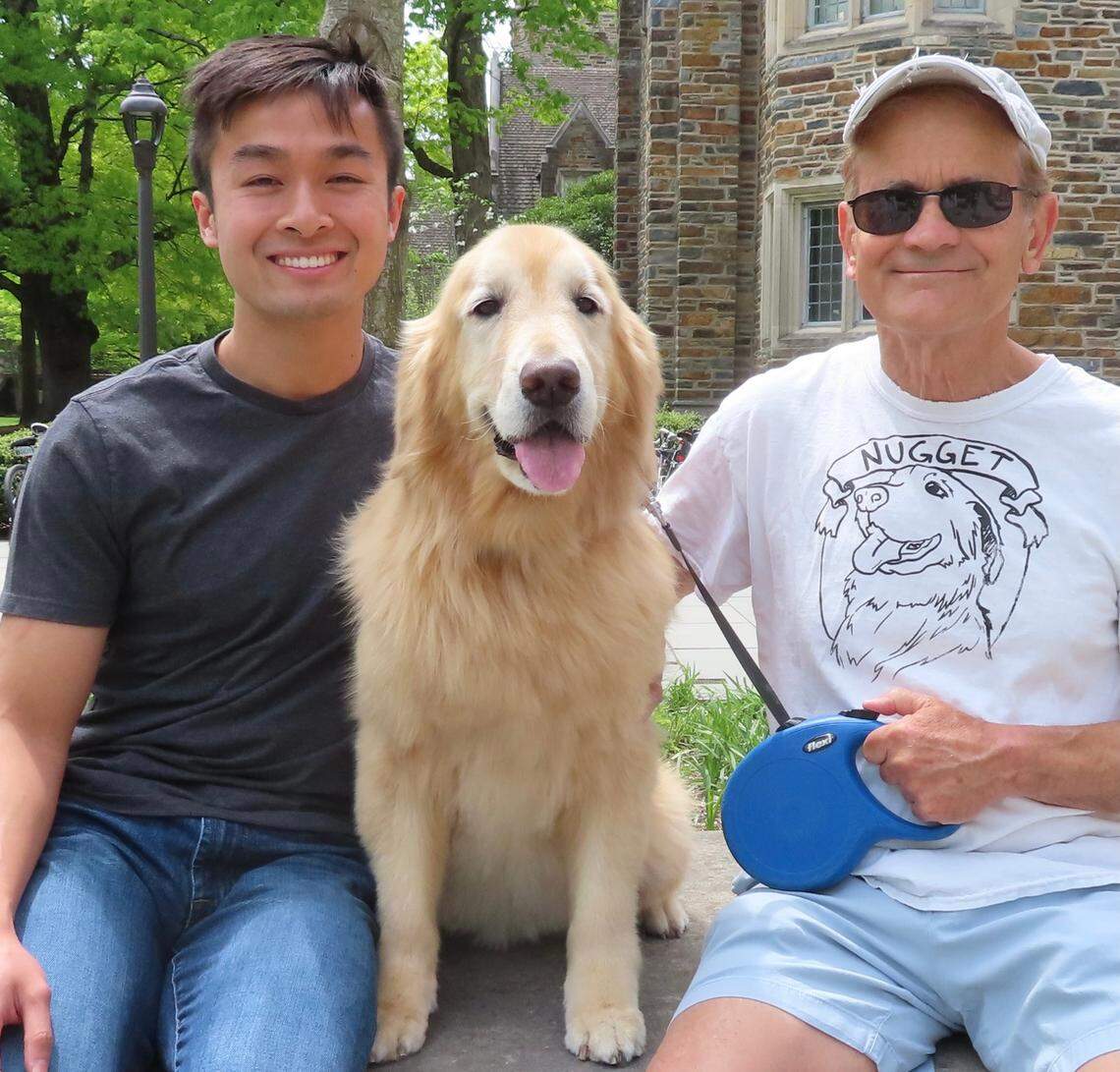 Duke University graduate Andrew Nguyen sits outside a Duke dining hall with Nugget and her owner Keith Upchurch who is wearing a custom Nugget T-shirt.