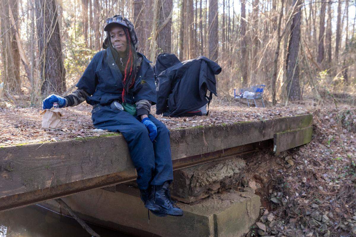 A woman who identified herself as “Sesame” drinks a beer on a footbridge in the woods near a camp where she lives next to the exit ramp from eastbound Interstate 40 onto South Saunders Street in Raleigh.