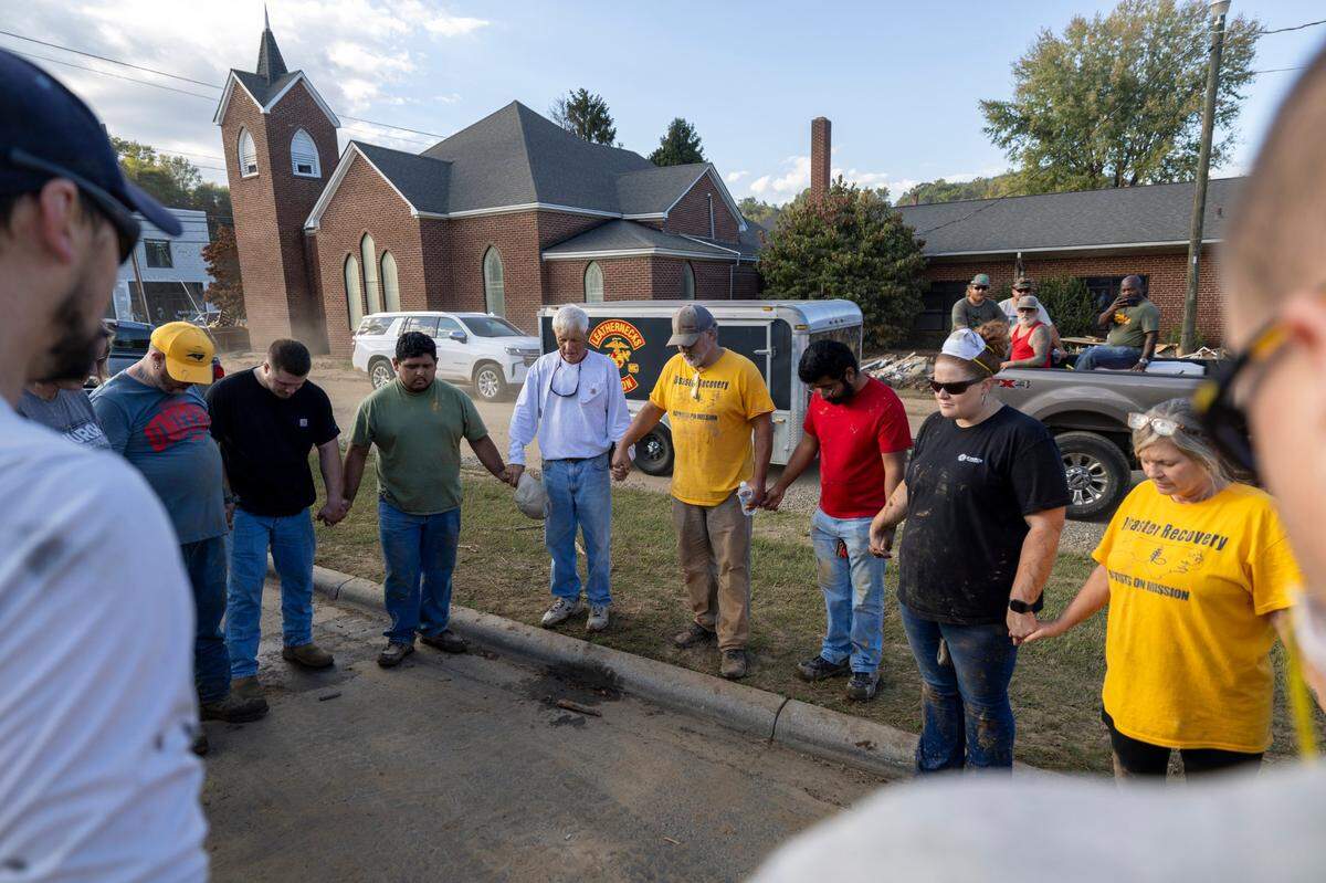 Members of IChurch from Hickory, N.C. pray with Bob Smith, center, a Trustee of the Old Fort United Methodist Church on Saturday, October 5, 2024 in Old Fort, N.C. More than four feet of water from Mill Creek flooded the building during Hurricane Helene. IChurch members volunteered their time on Saturday to shovel mud, and salvage items from the building.