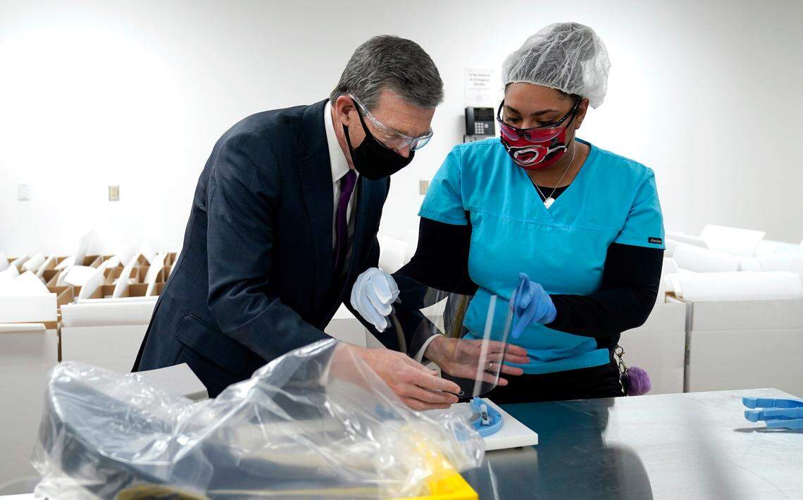 Gov. Roy Cooper, left, is assisted with assembling a face shield by employee Anne-Marie Dutch during a visit to Gilero in Pittsboro, N.C., Thursday, Dec. 3, 2020. The medical device manufacturer began producing face shields when the pandemic started and also produces swabs for rapid tests in addition to self contained oxygenated negative pressure environments.