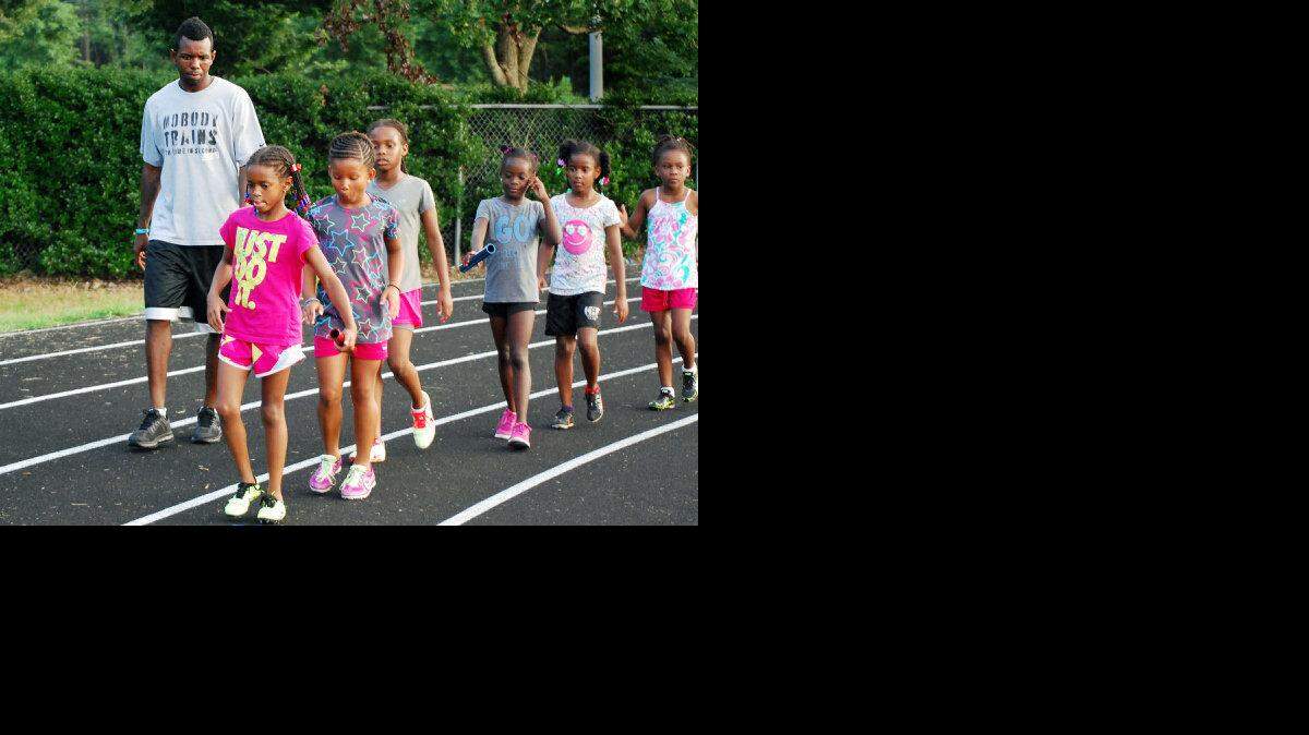Olympic medalist Bershawn Jackson, left, walks with members of the Carolina Elite Track & Field Club during a practice at Millbrook High School on Monday, July 22, 2013. Jackson is a sub-bantam coach for the Raleigh-based organization. His daughter Shawnti, front, competed with the club in the USATF Junior Olympic National Championships this week at North Carolina A&T.