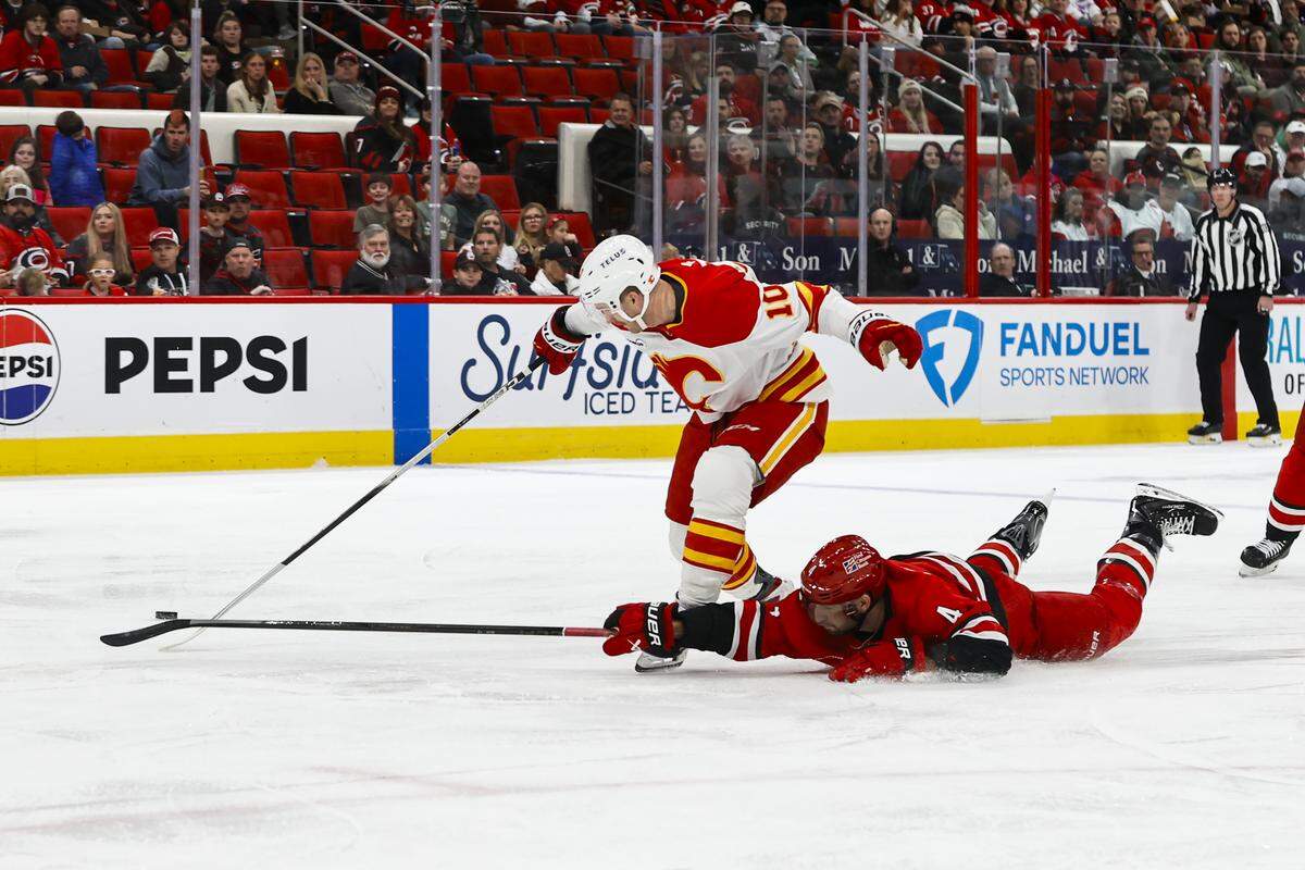 Shayne Gostisbehere of the Carolina Hurricanes dives to hit the puck away from Jonathan Huberdeau of the Calgary Flames during the first period at Lenovo Center on Nov. 30, 2025 in Raleigh, North Carolina.