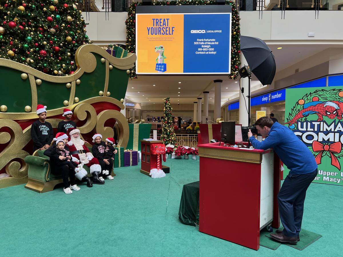 Cam Johnson (right) works for California-based Amuse Matte, running its Santa station at Crabtree Valley Mall. He said it’s the most successful set on the East Coast.”