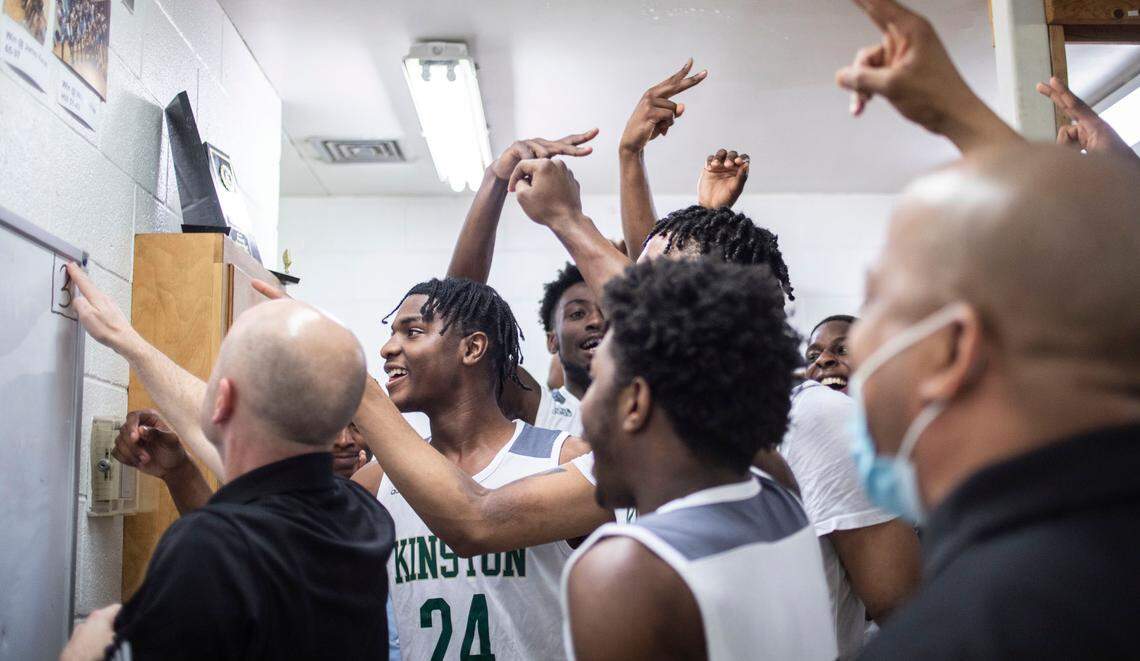 Kinston Vikings head coach Perry Tyndall starts to erase “3” from the team’s locker room white board after their playoff win on March 1, 2022 while players and assistant coaches hold up two fingers, signaling that the team has to play just two more games to win the state championship.
