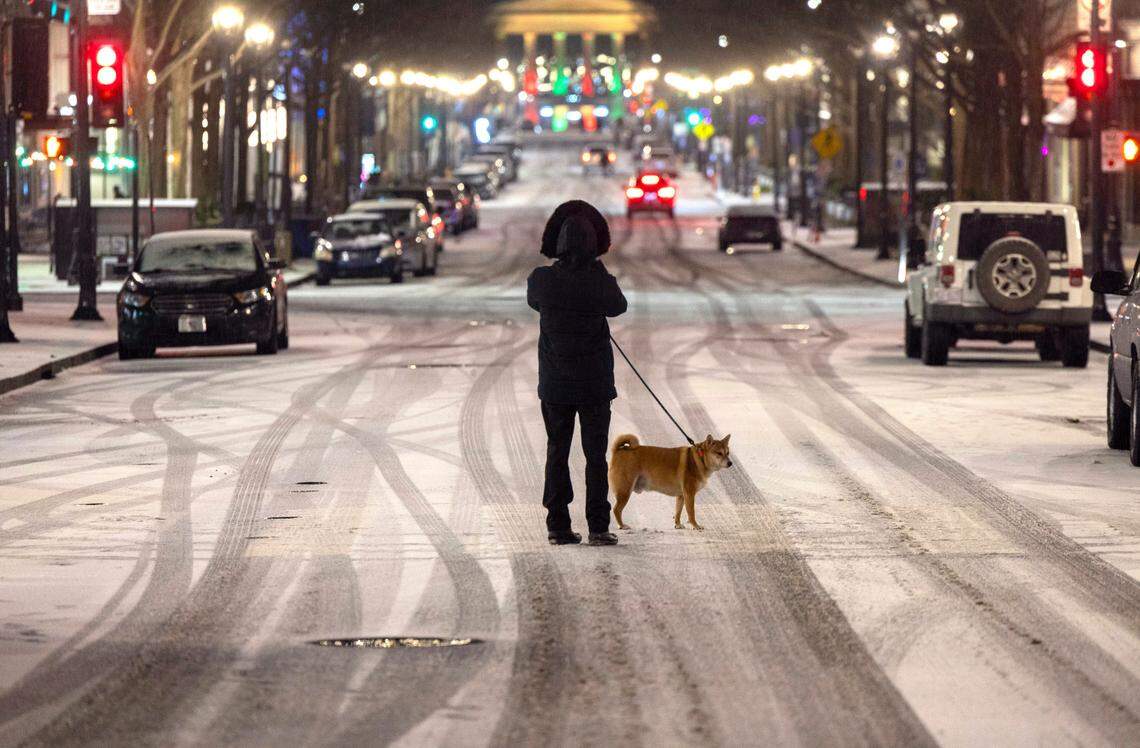 Matthew Smith pauses with his dog “Kobe” on Fayetteville Street to photograph the snow on Friday, January, 10, 2025 in Raleigh, N.C., after a winter storm moved across the state delivering a wintry mix.