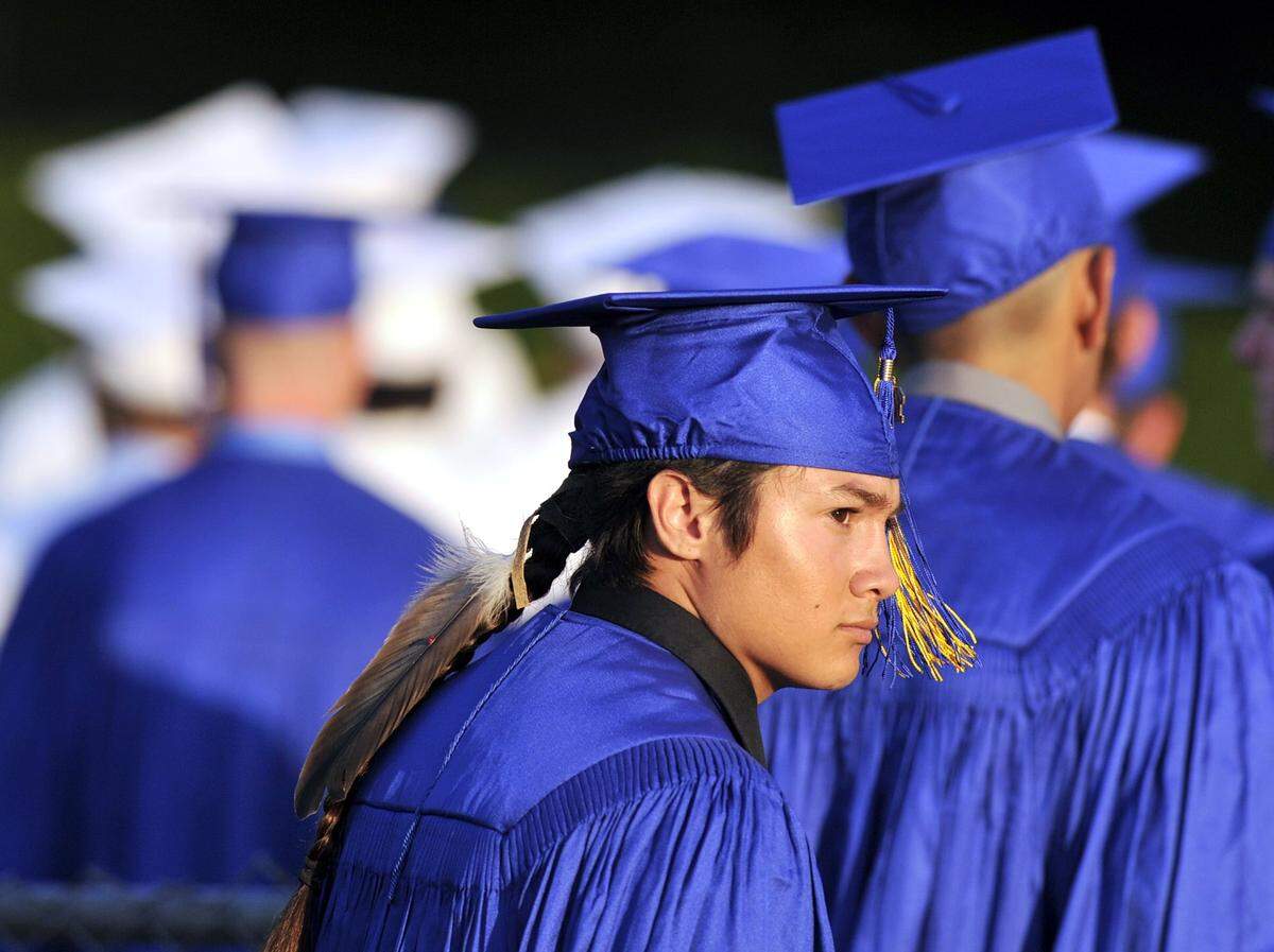 Christian Titman, center, looks into the sun wearing a feather as he and his graduating class enter Clovis High’s Lamonica Stadium in June 2015 in Clovis, Calif. North Carolina lawmakers are requiring public high schools to allow Native American students to wear bird feathers at graduation ceremonies.