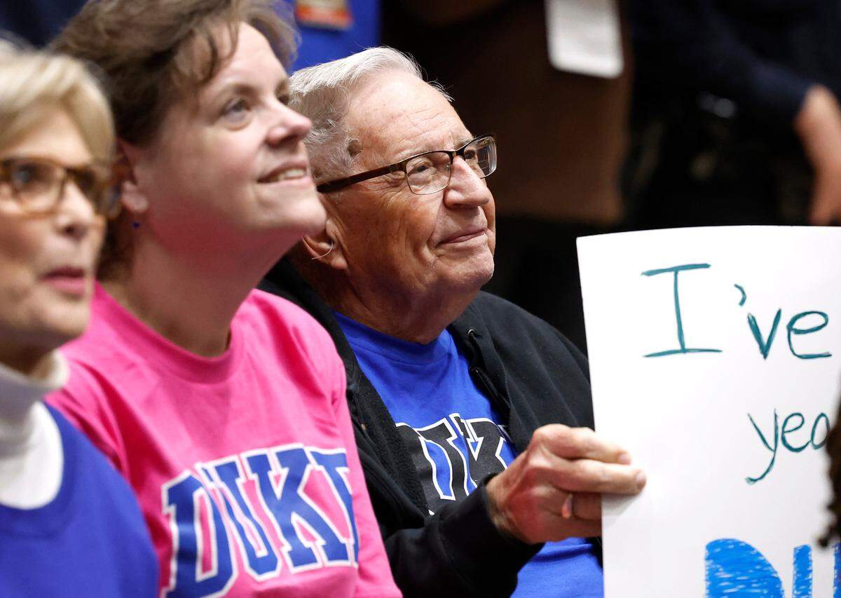 Holding a sign that states “I’ve waited 91 years for my first Duke game” is William Thompson, 91. Thompson attended the game against Queens on Saturday, Dec. 30, 2023, with his daughter, Shelley Thompson, center left, a Duke alumni.
