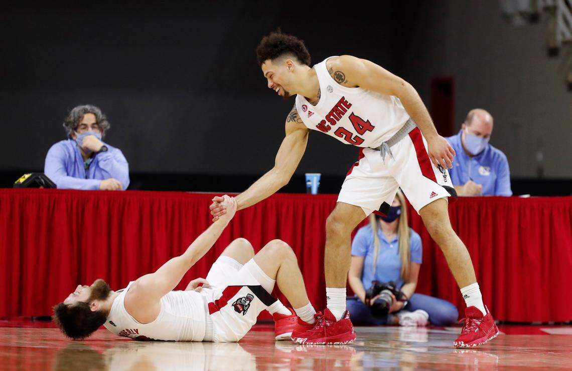 N.C. State’s Devon Daniels (24) laughs as he helps up Braxton Beverly (10) during the second half of N.C. State’s 79-76 victory over UNC at PNC Arena in Raleigh, N.C., Tuesday, December 22, 2020.