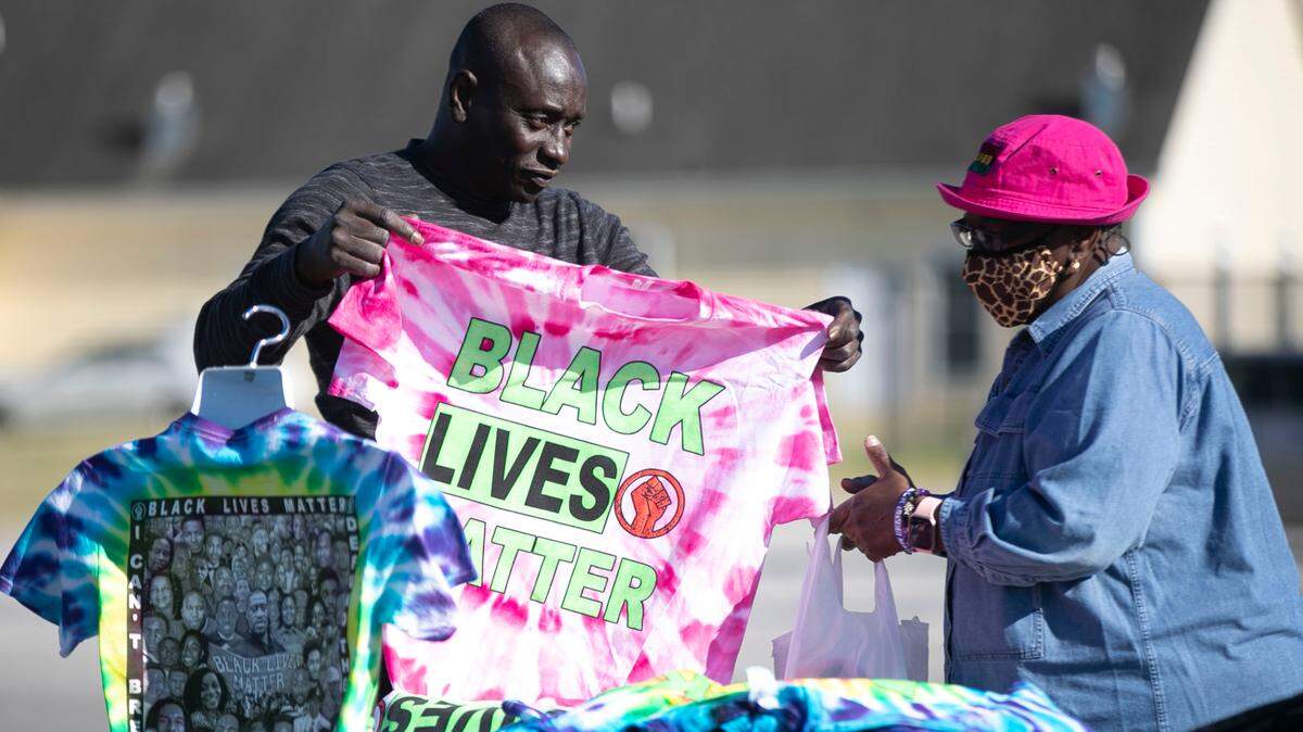 Casianne Beckford of Elizabeth City, N.C., purchases T-shirts from James Quattlebaum at his table along Ehringhaus Street on Saturday, May 1, 2021, in Elizabeth City, N.C. Quattlebaum, of Charlotte, N.C. has traveled all over the country selling t-shirts that protest police violence against Black people.
