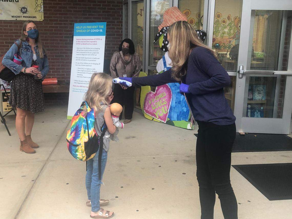 Nora Cline, a 1st-grade student, gets her temperature checked by Heather Barnes before entering Combs Elementary School in Raleigh, N.C., on Oct. 19, 2020. Her mother, Jen Cline, the school’s literacy coach, watches.