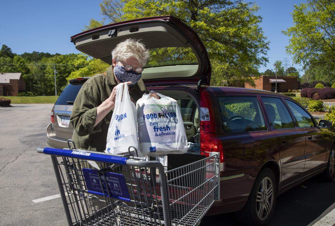 Wearing a homemade mask, Regina DeLacy transfers groceries from the cart to the car at Food Lion on Saturday, Apr. 18, 2020, in Durham, N.C. Durham County and City of Durham updated their stay-at-home order Friday evening to include new requirements to wear masks in public spaces where social distancing isn’t possible, such as the grocery store, starting Monday at midnight.