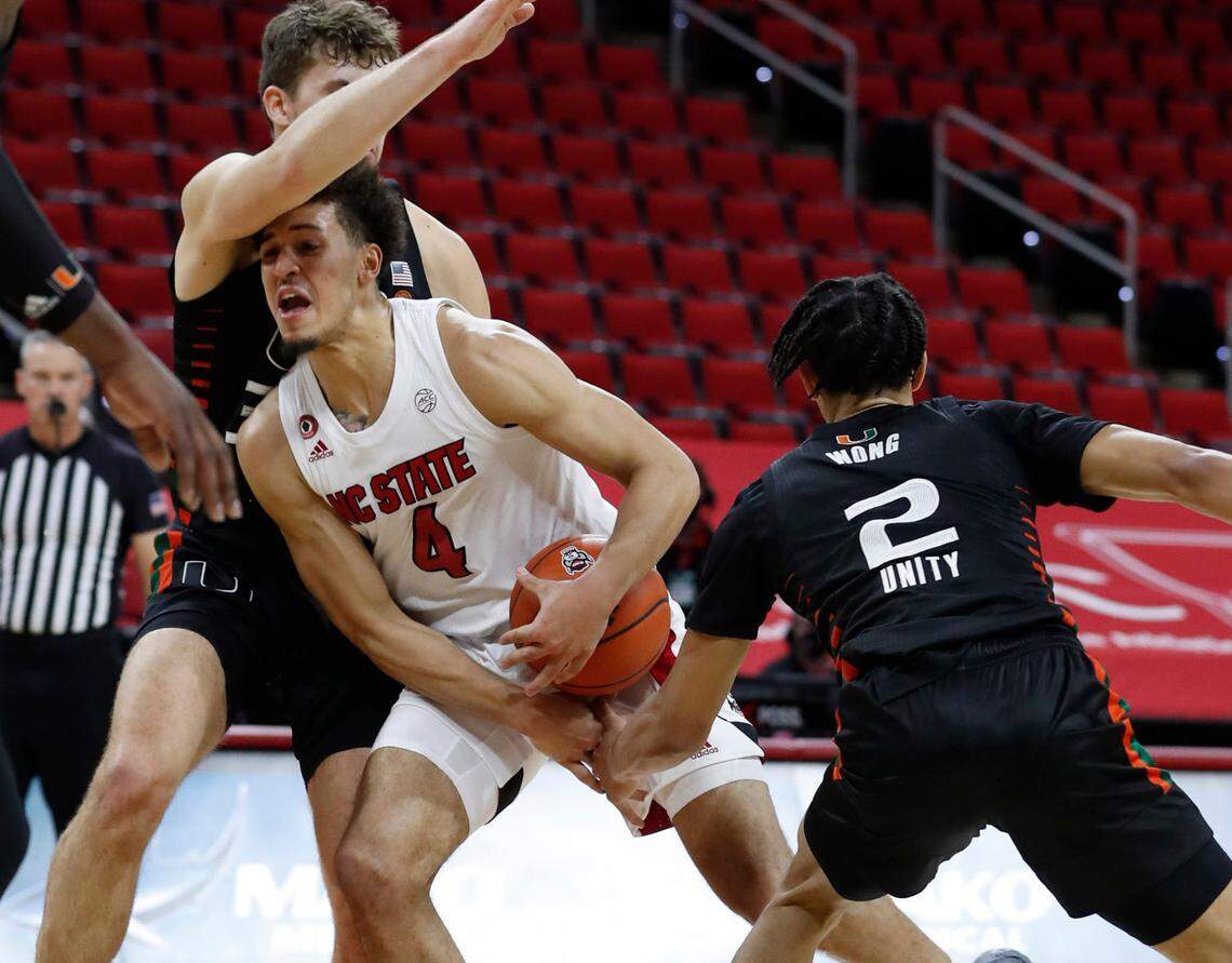 N.C. State’s Jericole Hellems (4) drives by Miami’s Matt Cross (33) and saiah Wong (2) during the first half of N.C. State’s game against Miami at PNC Arena in Raleigh, N.C., Saturday, January 9, 2021.