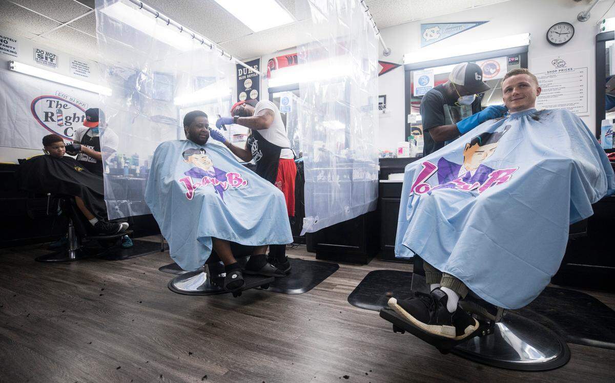 Barbers at Right Cut Barber Shop in Cary, N.C., wear masks and gloves while being separated by shower curtains as they work with clients on Saturday morning, May 23, 2020. Customers have been calling and booking appointments nonstop since the shop opened as a part of Phase Two of reopening North Carolina.