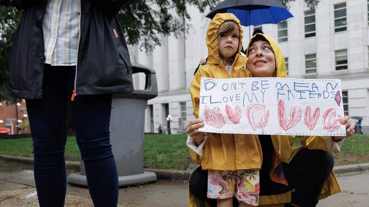 Marie Garlock smiles at her daughter, Soma Synowiez, 4, as they together hold a sign during a Moral Monday demonstration at the North Carolina State Capitol on Monday, Sept. 29, 2025, in Raleigh, N.C. Speakers at the event described how potential cuts to Medicaid could affect North Carolinians. Garlock said the two attended the gathering to honor her mother, who was diagnosed with cancer in a healthcare coverage gap.