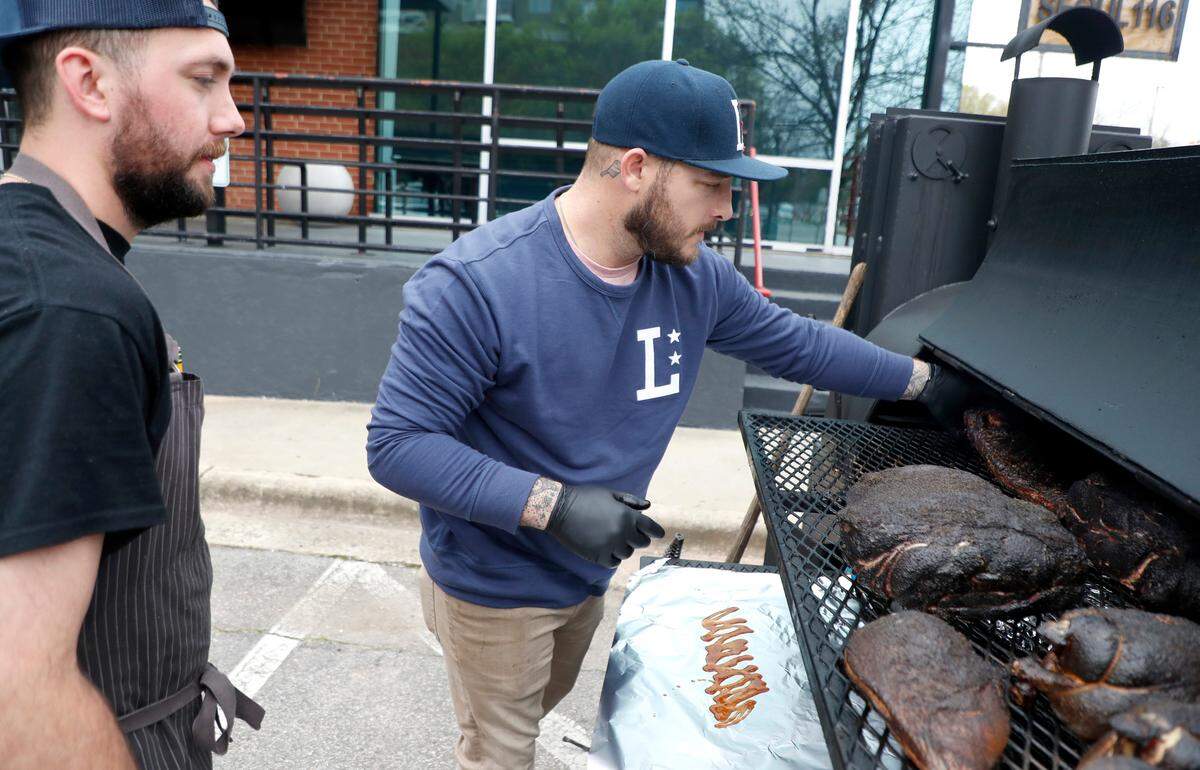Jake Wood, owner of Lawrence Barbecue, checks on ribs that are being cooked in a smoker Thursday, March 26, 2020. Wood, working from a smoker in a parking lot on North West Street in Raleigh, N.C., is offering no-contact take out barbecue meals for the public and free meals for those in the service industry. To the left is Eddie Forbis, chef de cuisine of Lawrence Barbecue.