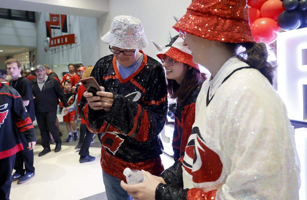 From left, Earl Saito and his daughters Shelly and Allison look over a photo of them taken in the concourse before the HurricanesÕ game against the Golden Knights in the second game of the Stanley Cup Final at the Lenovo Center in Raleigh, N.C., Thursday, June 4, 2026.
