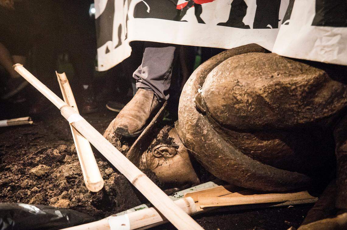A toppled Silent Sam lays face down in the dirt Monday, Aug. 20, 2018, at UNC-Chapel Hill. Demonstrators surrounded and obscured the statue with large banners before toppling it.
