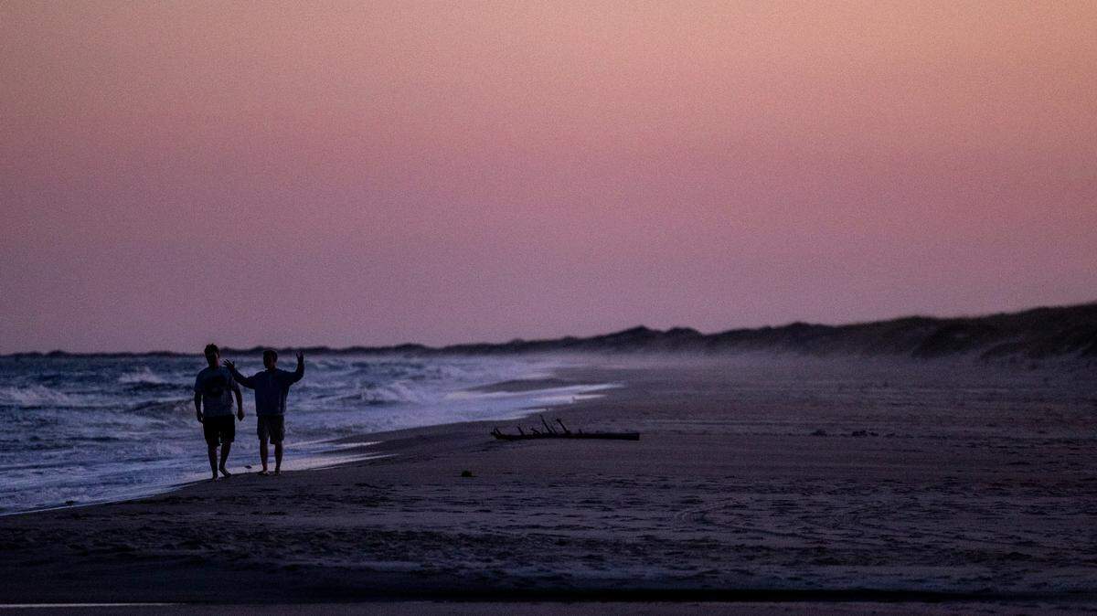 Beachgoers walk along the Cape Hatteras National Seashore in Ocracoke as the sun sets Tuesday, May 17, 2022. Hyde County is among the 29 North Carolina school districts listed in a state report as not following the school calendar law.