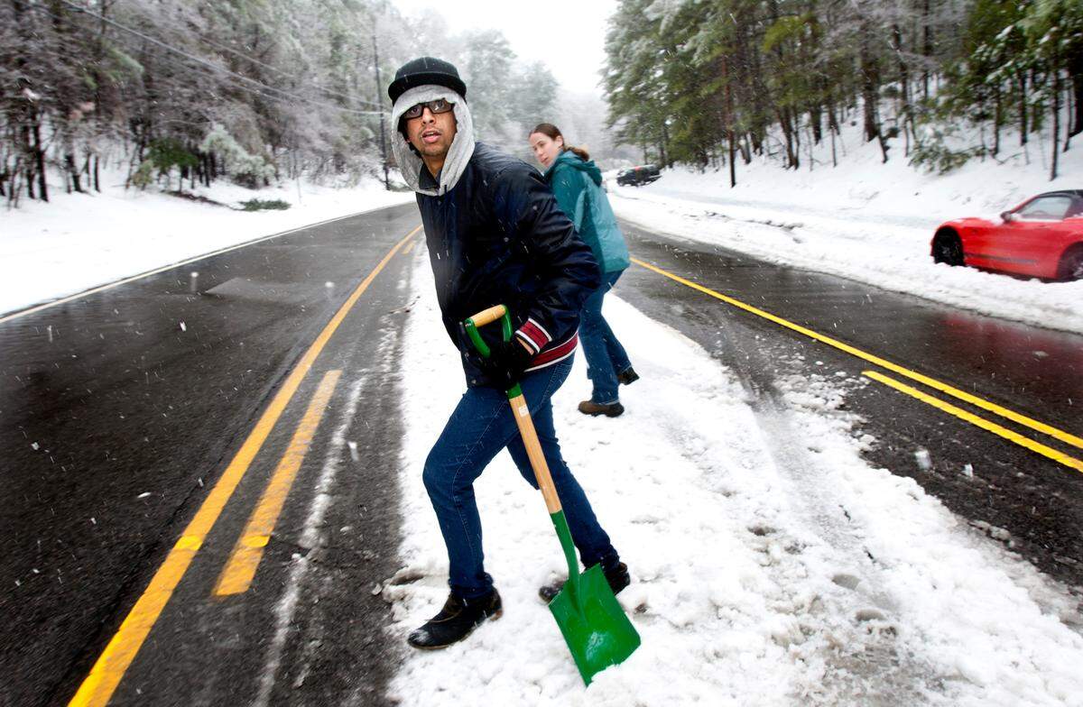 After lending her shovel to one motorist to move his stranded vehicle off of Avent Ferry Road in Raleigh, Ashley Jermusyk, rear, then leaves her shovel with another stranger, Sam Almheiri, a freshman at NC State and from Hawaii, front, on Thursday, February 13, 2014. He also had to leave his car overnight on Wednesday and walk home. They made arrangements for her to pick it up at a later time. Area residents begin to dig out on the second day of snow in the Triangle region.