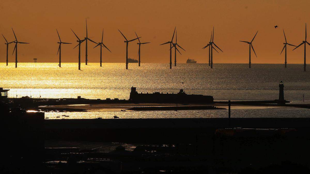 The sun sets over Burbo Bank Offshore Wind Farm on the River Mersey behind Fort Perch Roick and New Brighton Lighthouse, in Liverpool, England.