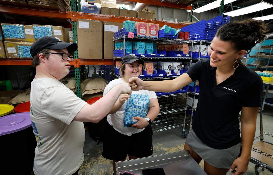 Paul Kocher fist-bumps Lindsay Wrege at the 321 Coffee roasting facility in Raleigh, N.C., Tuesday, June 25, 2024. With them is Sophie Pacyna.