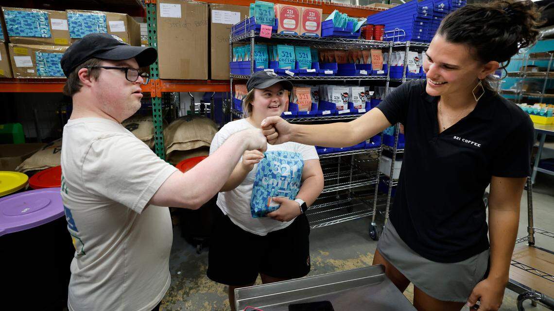 Paul Kocher fist-bumps Lindsay Wrege at the 321 Coffee roasting facility in Raleigh, N.C., Tuesday, June 25, 2024. With them is Sophie Pacyna.