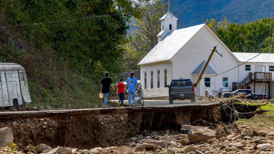 A family in the Pensacola community of Yancey County, N.C. carry milk and food to their home after picking them up at the community fire department on Thursday, October 3, 2024. The area has been heavily damaged from Hurricane Helene, with the roads in inaccessible due to flooding.