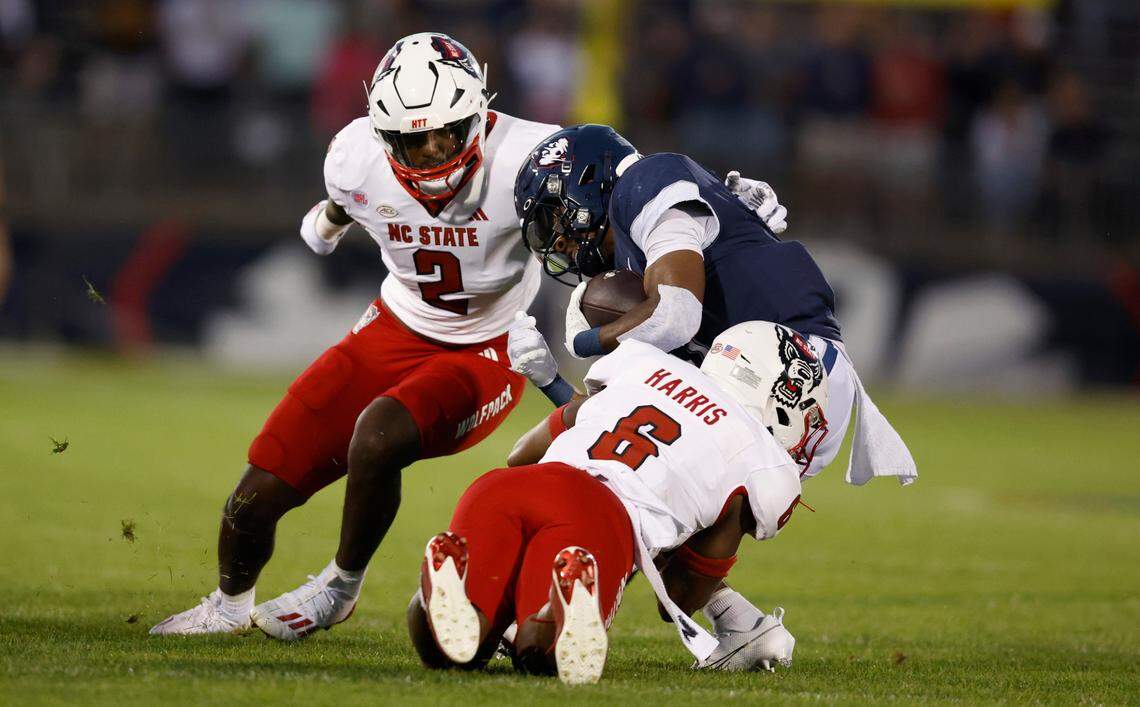 N.C. State’s Jakeen Harris (6) and Jaylon Scott (2) tackle Connecticut running back Devontae Houston (1) during the first half of N.C. State’s game against UConn at Rentschler Field in East Hartford, Conn. Thursday, August 31, 2023.