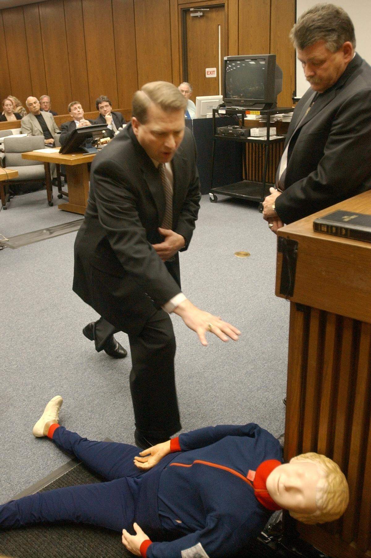 District Attorney Jim Hardin, center, asks Dan George, Identification Technician with the Forensic Service of the Durham City Police Department, right, how he saw Kathleen Peterson’s body and show how Michael Peterson went to hug his deceased wife, Kathleen, on the night she died during testimony July 18, 2022.