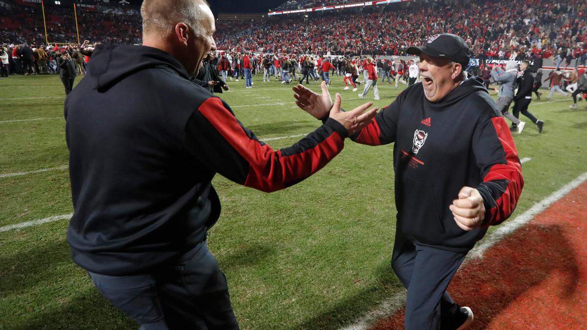 N.C. State head coach Dave Doeren and defensive line coach Charley Wiles celebrate after N.C. State’s 34-30 victory over UNC at Carter-Finley Stadium in Raleigh, N.C., Friday, November 26, 2021.